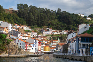 Fototapeta na wymiar Traditional fishing village pictured from the sea. Natural harbor between the hills of the coastline. White houses with orange roofs. Colorful buildings. Cudillero, Asturias, North of Spain