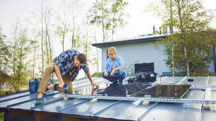 Father and Son Installing Solar Panels to a Metal Basis. They Work on a House Roof on a Sunny Day. Concept of Ecological Renewable Energy at Home and Quality Family Time.