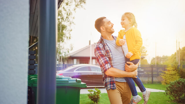 Happy Father Holding A Young Girl. They Threw Away Trash Into Correct Garbage Bins Because This Family Is Sorting Waste And Helping The Environment. Shot With Warm Sun Flare.