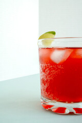 Red sparkling drink in the glass with ice and lime