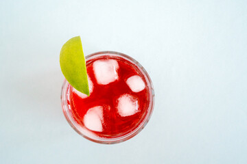 Red sparkling drink in the glass with ice and lime
