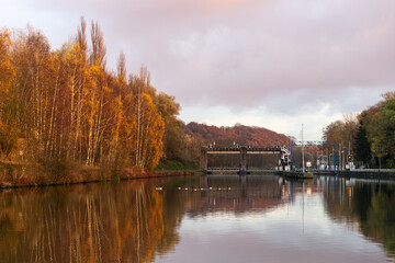 Fototapeta premium Ship lock on the river with yellow autumn trees along the shore and wild geese floating on the water