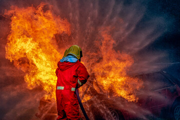Firemen fighting raging fire with huge flames of burning and fuel explosion.Firefighter spraying water using extinguisher and water for spraying water make water barrier to fighting and control fire .