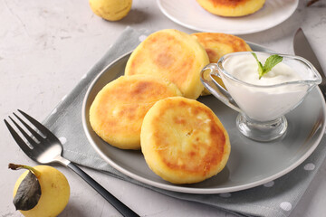 Homemade traditional Ukrainian dish syrniki with sour cream on grey plate on light background, Cottage cheese pancakes
