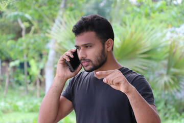 Serious bearded young man having phone conversation, gesturing with hand as trying to explain something, solving problems via smartphone on distance