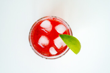Red sparkling drink in the glass with ice and lime