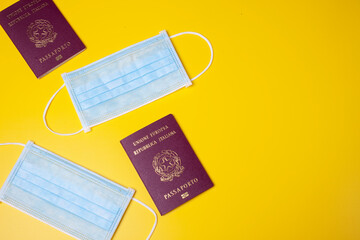 blue medical facial mask  on a yellow background and italian passports. Travel in the age og...