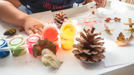 Toddler boy is home schooled paiting yellow leaves and pine cones in fall with eco friendly paint. Sensorial activity at home.