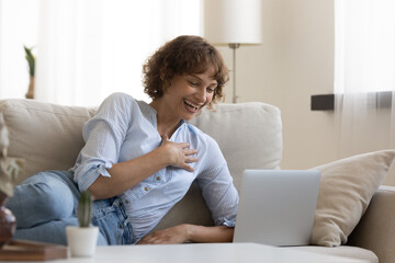 Fototapeta premium Overjoyed young Caucasian woman relax on couch in living room have fun talking on webcam virtual call on laptop. Happy female rest on sofa laugh smile watching funny video online.