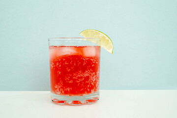 Red sparkling drink in the glass with ice and lime