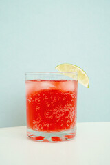 Red sparkling drink in the glass with ice and lime