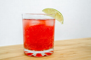 Red sparkling drink in the glass with ice and lime