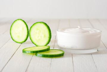 Moisturizer with cucumber slices on white wooden