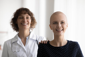 Portrait of smiling young sick hairless female cancer patient and caring nurse look in future recovery together. Doctor support optimistic ill bald woman suffering from oncology. Medicine concept.