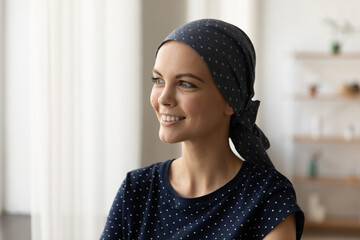 Smiling young Caucasian sick woman with scarf on head suffer from oncology look in distance dream...