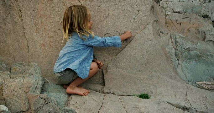 A preschooler is drawing on a rock wall on the beach with charcoal