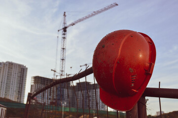 orange bright helmet hangs on the fence. in the background a construction gantry crane for moving...