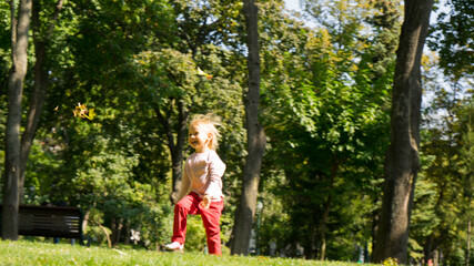 Naklejka na ściany i meble Portrait of cute beautiful blonde baby girl with big blue eyes and open mouth.Surprised or scared little european girl.Child standing isolated in the park.Childhood concept