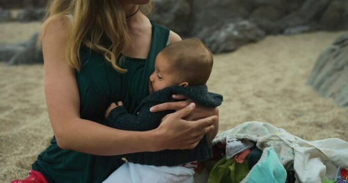 A young mother is breastfeeding her baby on the beach in summer at sunset
