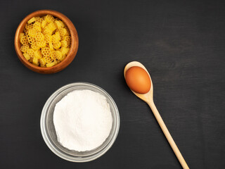 Pasta, flour and egg in spoon on a black wooden background