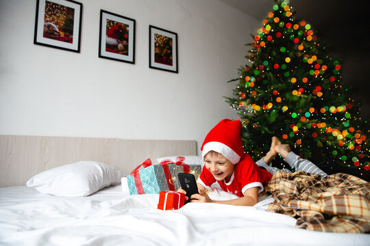 Christmas activity indoor: new year's online greetings and meetings. Boy in santa hats look at a tablet and communicate with grandparents. Anticipation of the holiday.