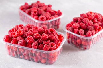 Fresh raspberry in plastic boxes on light background