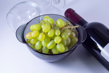 Green grapes, empty glass and bottle of wine on a white background.