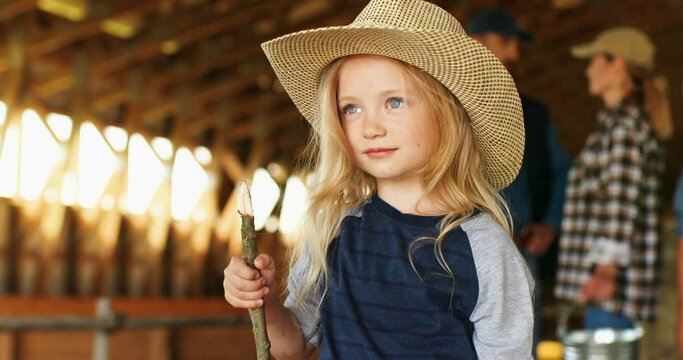 Portrait shot of cute funny Caucasian pretty firl with blonde hair in hat standing in shed and smiling cheerfully. Close up of beautiful joyful kid laughing in stable at farm. Summer in countryside.