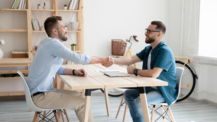 Smiling hr manager wearing glasses shaking candidate hand on interview, greeting or congratulating, two business partners handshake, making agreement, signing contract, making successful deal
