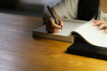 part of young female holding pen reading book at night. Defocused background