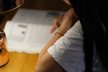 over shoulder view of young woman reading book under lamp light at night