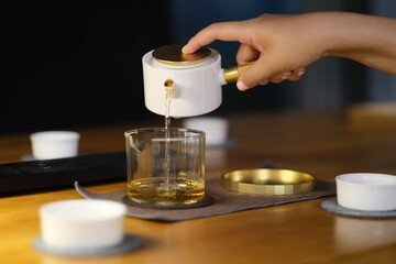 close up hand pouring tea water from traditional Chinese teapot to fair mug. Defocused background