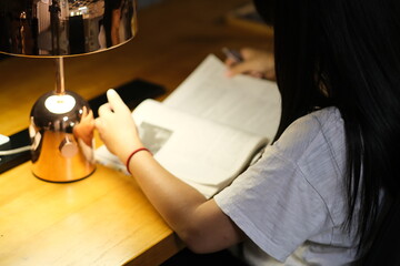 over shoulder view of young woman reading book under lamp light at night