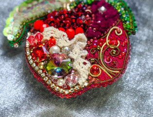 Decorative red apple made of beads, sequins and lace on a gray background