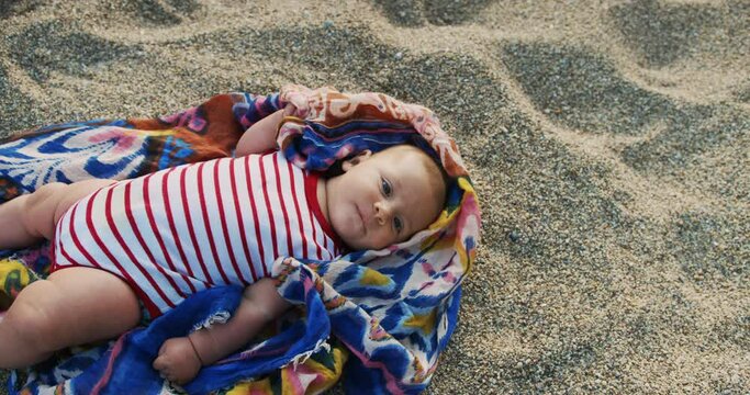 A little baby is lying on the beach at sunset
