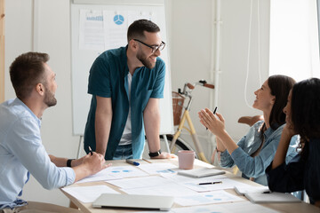 Smiling confident businessman mentor wearing glasses leading corporate meeting, standing in modern boardroom, training diverse staff, diverse employees listening to team leader, applauding