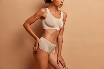 Body care and beauty concept. Unrecognizable dark skinned woman in underwear stands against brown...