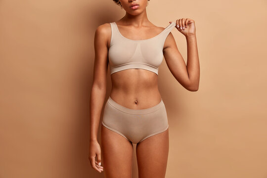 Femine beauty lines concept. Slim woman with dark skin flat stomach wears high waist panties and bra. Female model poses in underwear against brown background