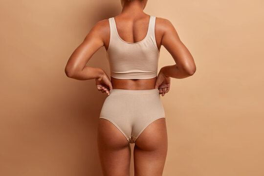 Back view of sensual slim woman poses in panties and top has perfect figure healthy dark skin isolated on brown background. Perfect female body