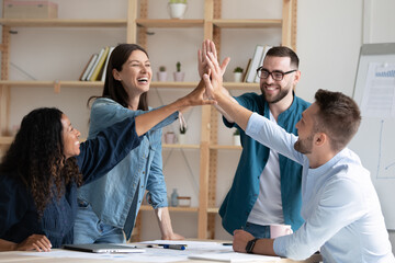 Overjoyed diverse employees giving high five at corporate meeting, excited colleagues joining...