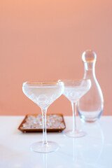  glass decanter, elegant glasses with cocktail and ice on beige background. Alcohol, water, party, hotel, bar concept