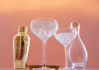 golden shaker, glass decanter, elegant glasses with cocktail and ice on beige background. Alcohol, party, hotel, bar concept