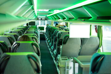 Modern tourist bus with green backlight and big white screen with copy space. Empty aisle of...