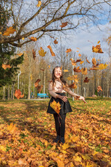 A cheerful girl throws up fallen leaves in the park.