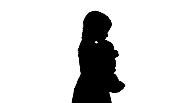 Silhouette Little girl in polka dot dress hugging big teddy bear while walking and looking at camera.
