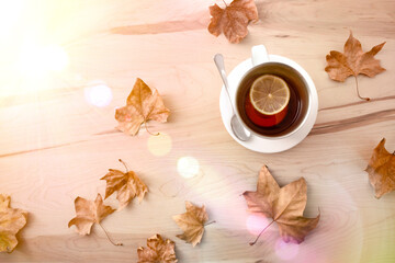 Tea with lemon on wooden table with leaves sunny top