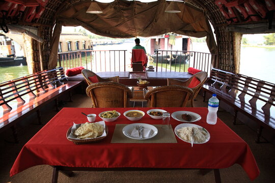 View of a houseboat furnished with an open lounge and food severed on table sailing on the Kerala backwaters in Alleppey, Kerala, India