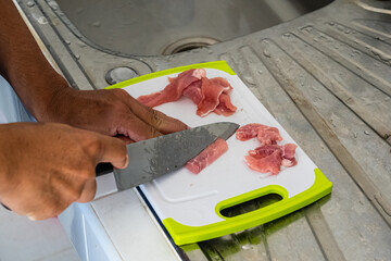 Some pieces of red pork were placed on a plastic cutting board. to be cut into thin slices, prepared for cooking.