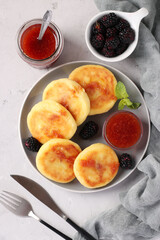 Homemade traditional Ukrainian dish syrniki with berry jam and blackberry on grey plate on light background, Top view