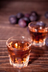 Plum vodka or brandy with fresh plums on the wooden table.
